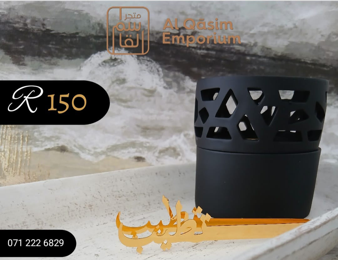 Black bakhoor burner with gold incense stick holder on a marble surface, branded 'Al Qasim Emporium'.