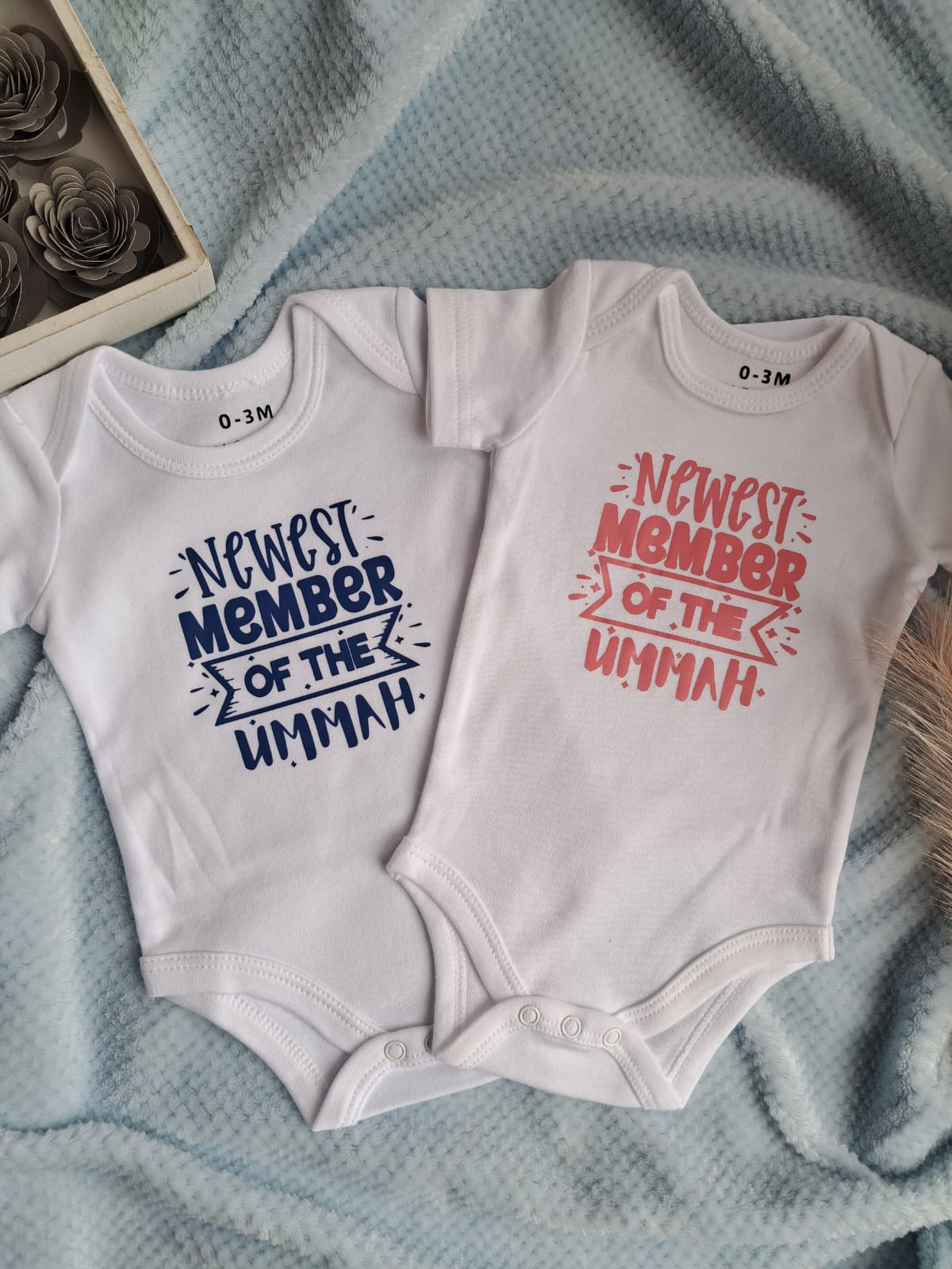 Two baby onesies with text on a textured surface