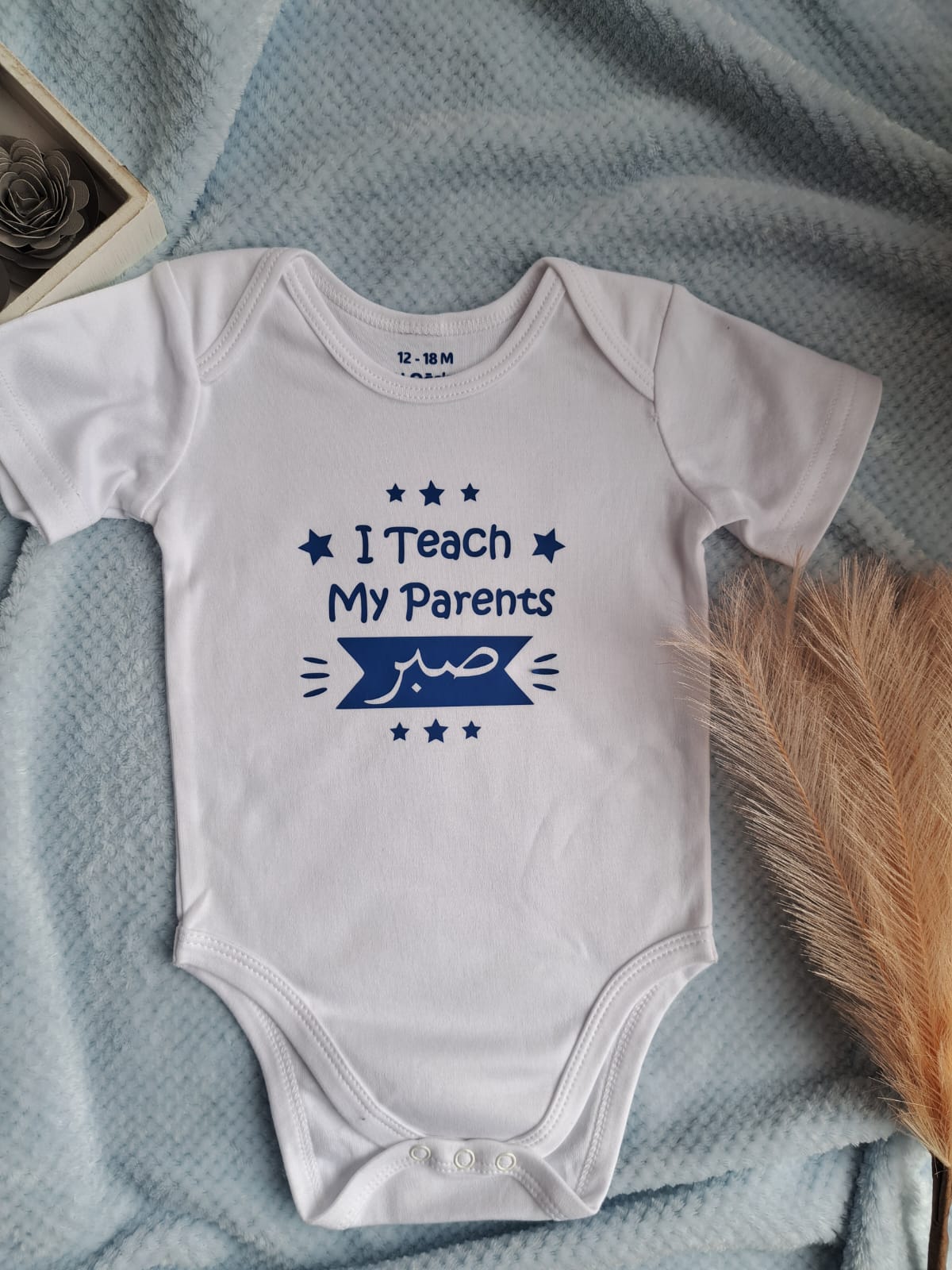 White baby onesie with blue text on a textured surface